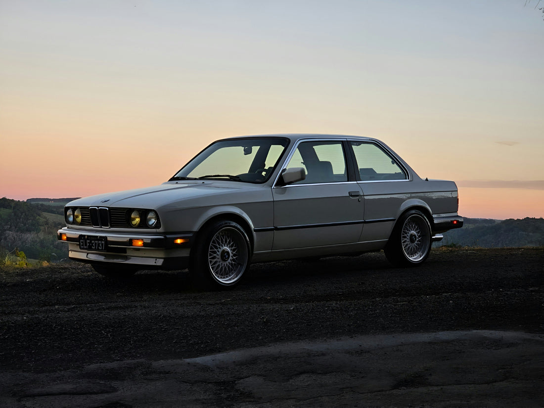 Silbernes BMW E30 Coupé bei Sonnenuntergang auf einem Aussichtspunkt